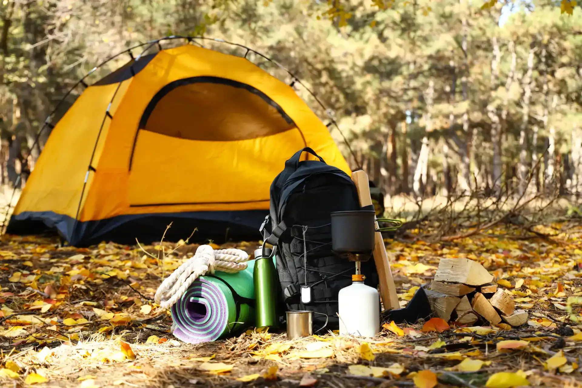 yellow camping tent pitched in a forest surrounded by hiking supplies